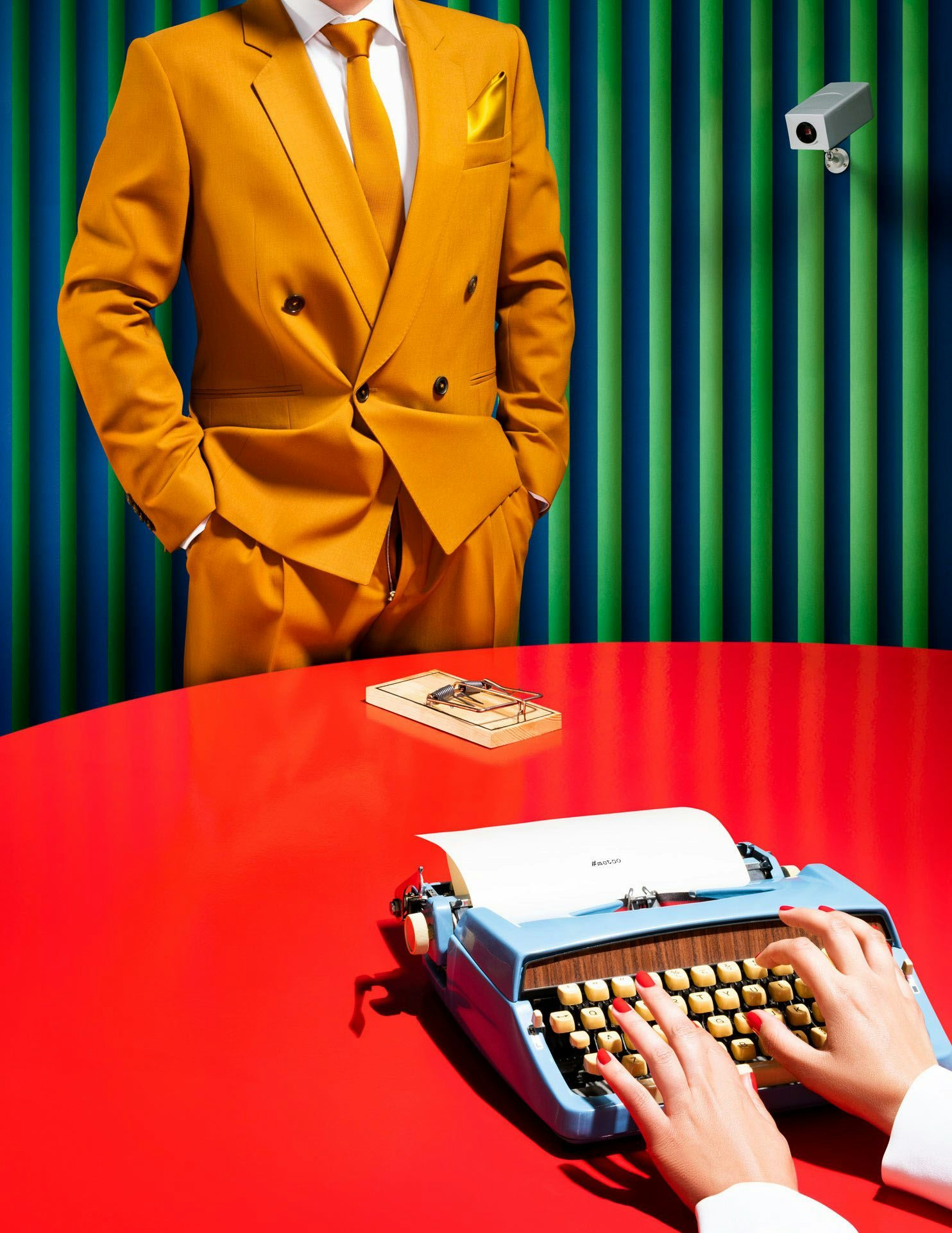 A headless figure in a bright orange suit stands before a green and blue striped wall, with a close-up of hands typing on a vintage typewriter on a red table.