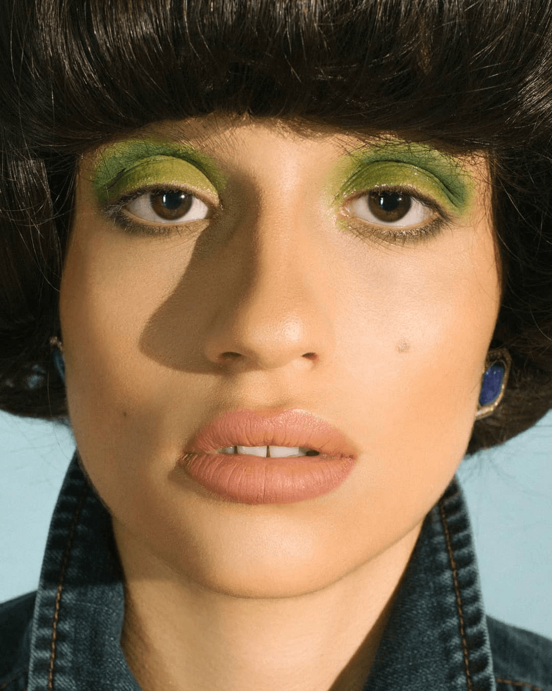 A close-up of a woman's face with vibrant green eyeshadow, capturing a vintage look with modern makeup artistry.
