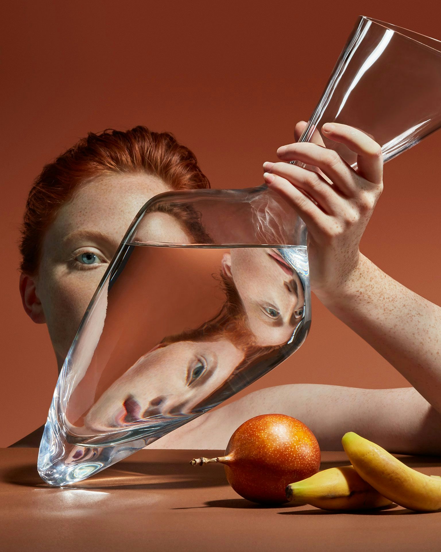 A woman's face refracted through a water-filled vase she holds.