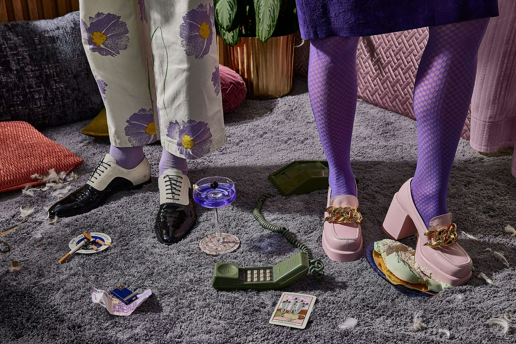 Lower legs of two in retro chic clothes, one stepping on a macaron on an elegant carpet.