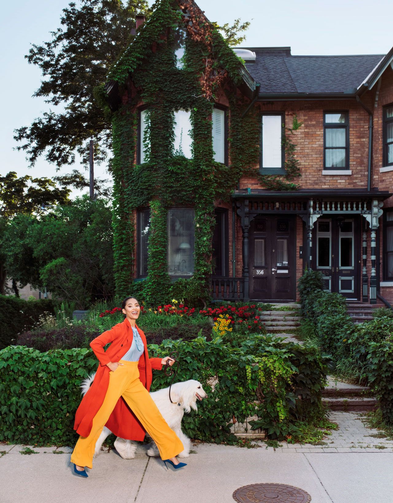 A vibrant shot featuring a person walking a fluffy white dog, both beaming with joy. The scene is set against an ivy-covered house with a charming, colorful garden.