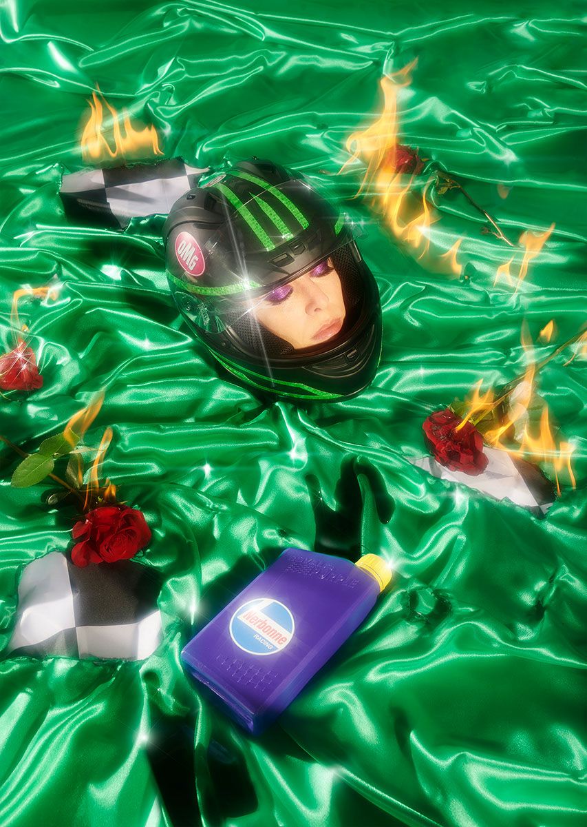 A surreal image of a woman's head in a racing helmet, lying on a green satiny fabric with flames, roses, and a bottle of motor oil.